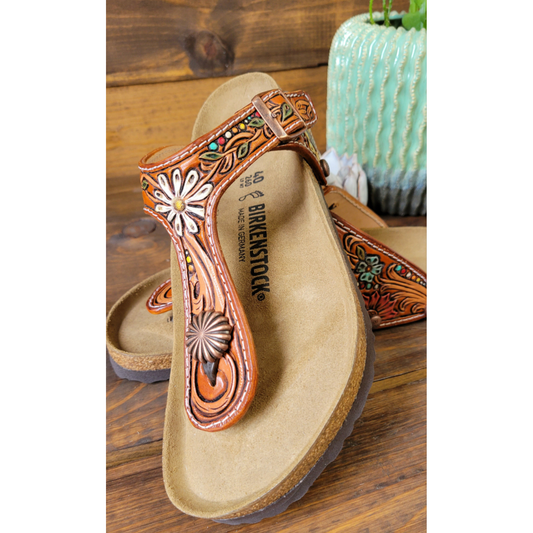 Handcrafted sandal with floral designs on a wooden surface.