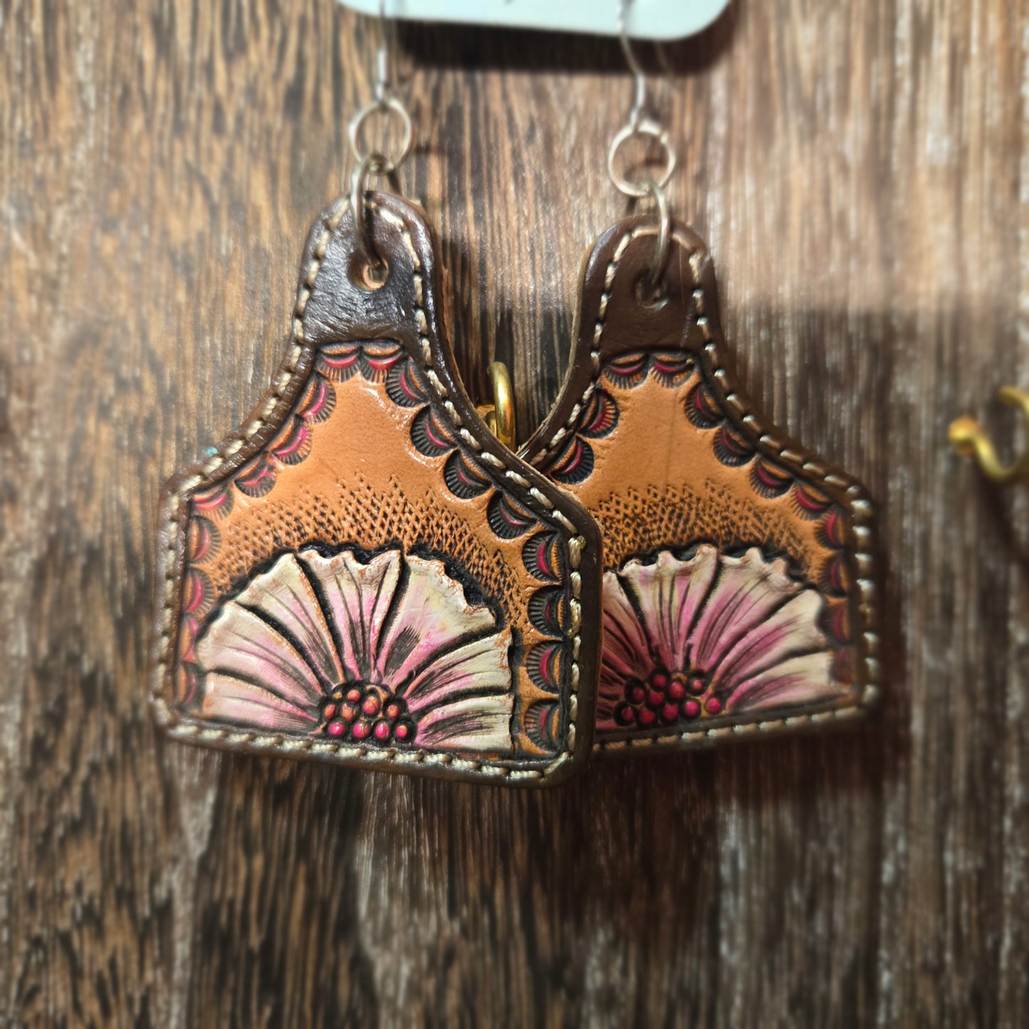 A pair of hand-tooled leather earrings with floral designs, resting on a rustic wooden surface.