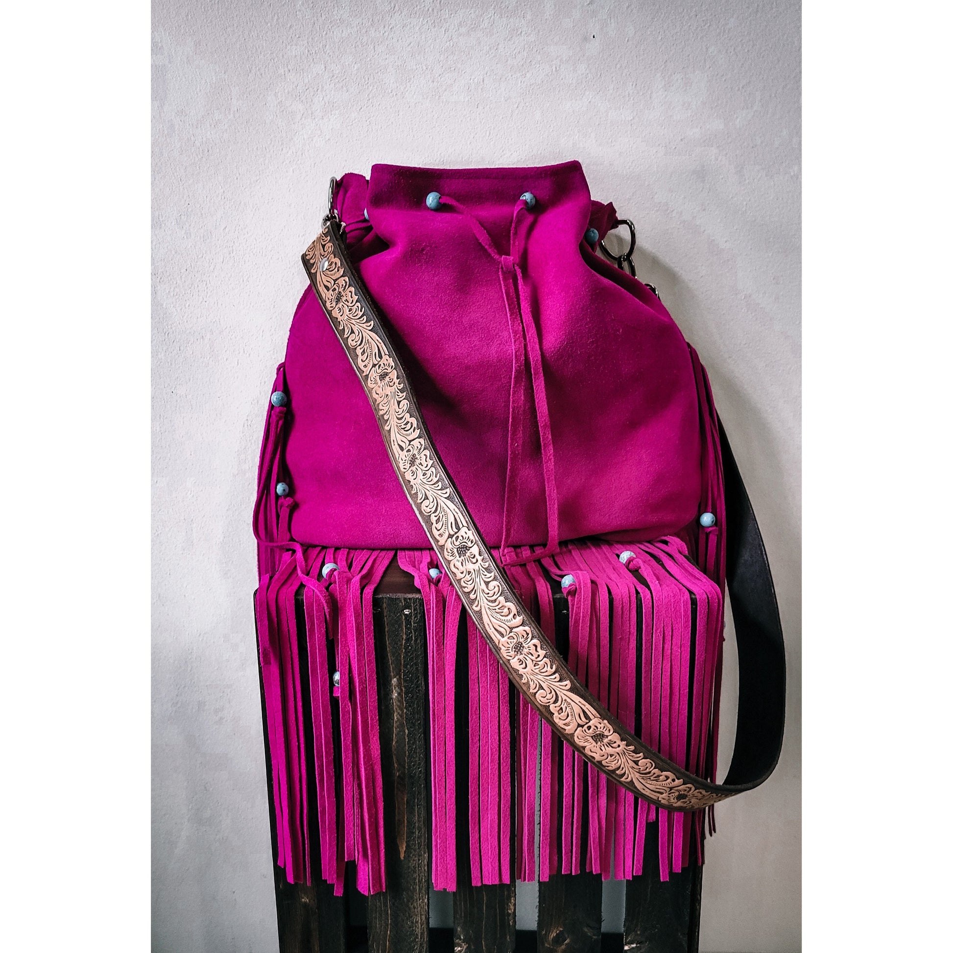 Bold and Beautiful fuchsia suede western fringe bag with turquoise bead accents and tooled adjustable strap that is a custom add on, shown closer up on a rustic wood old pallet