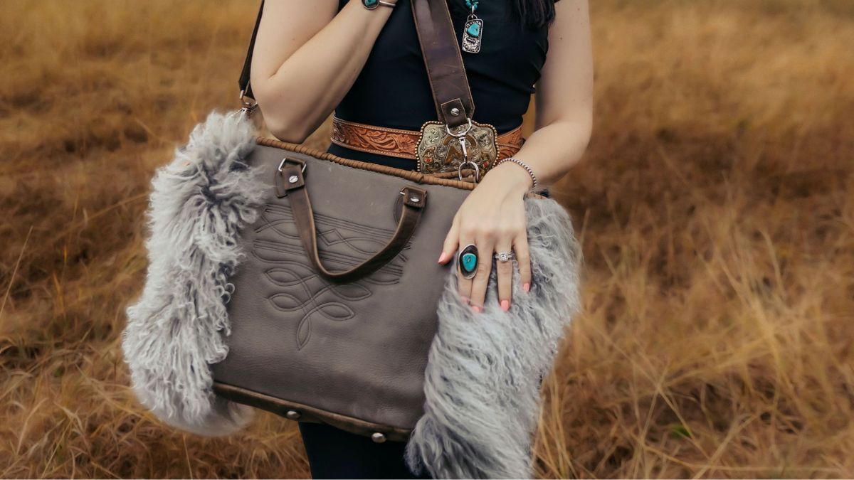 Person holding a brown leather bag with fur trim in a field made by J.Huber Leather Designs
