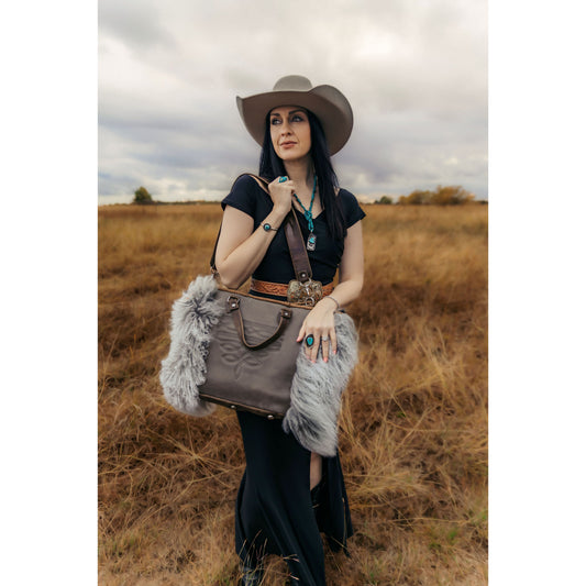 Woman in a field holding a gray leather handbag with fur accents