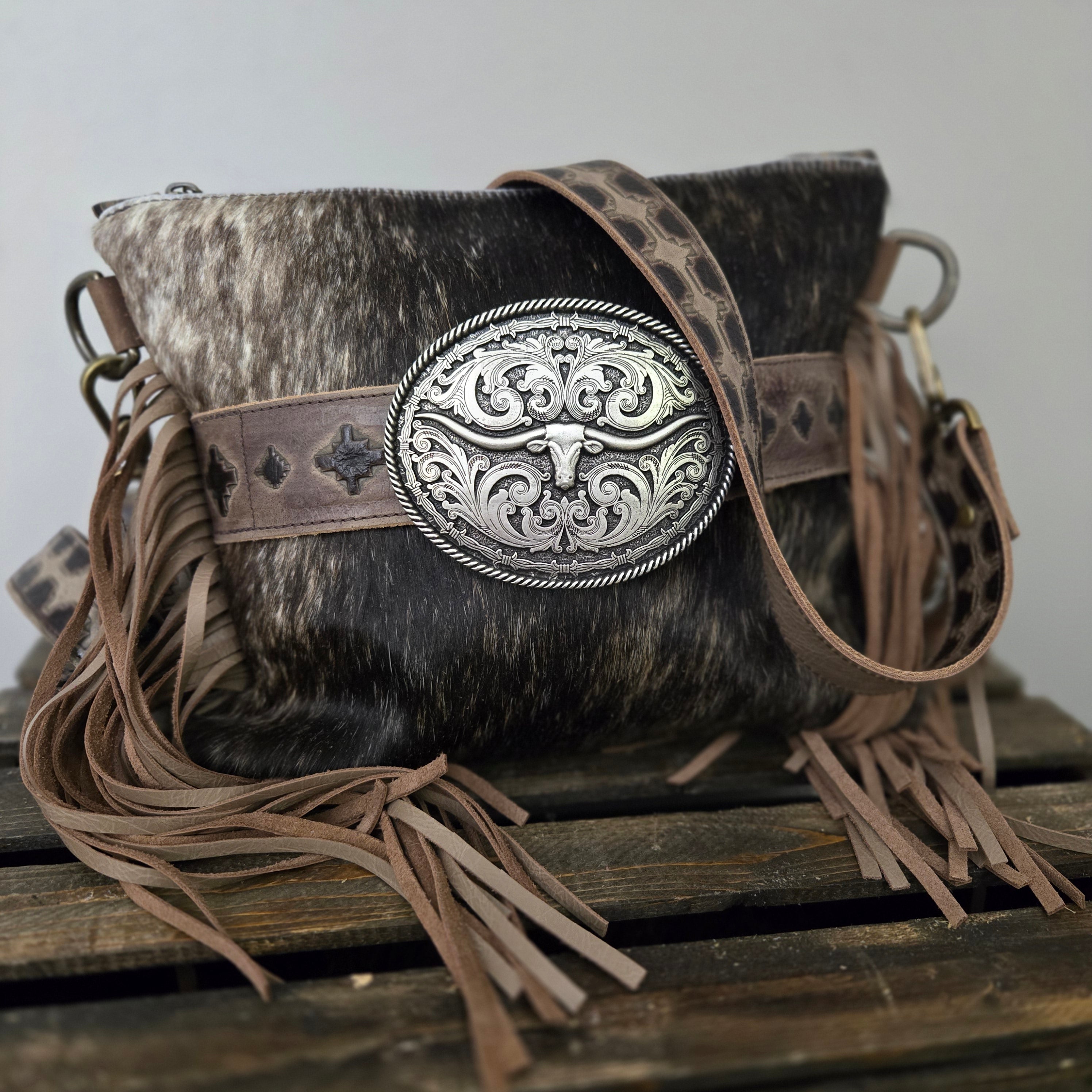 Cowhide leather pouch with decorative silver buckle and fringes on a plain background