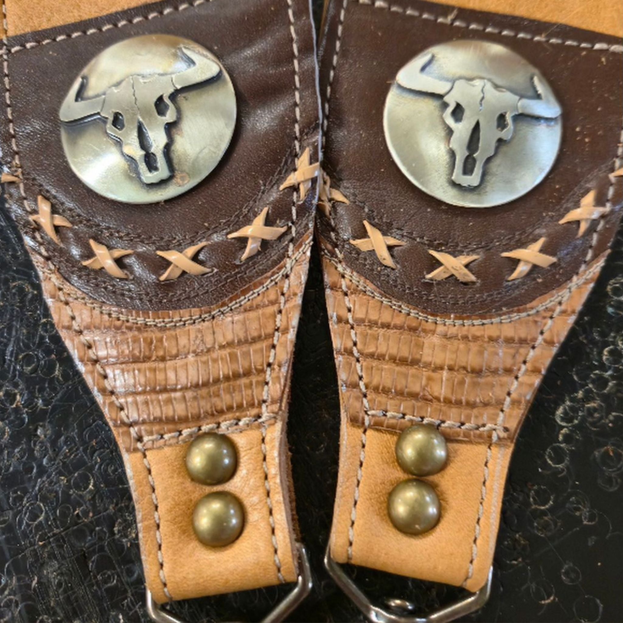 leather bag straps with longhorn buttons on dark background